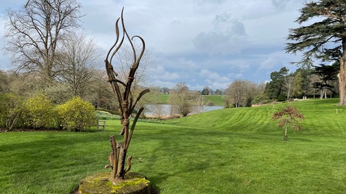 spring garden view with a curving metal sculpture in the foreground and a lake in the background